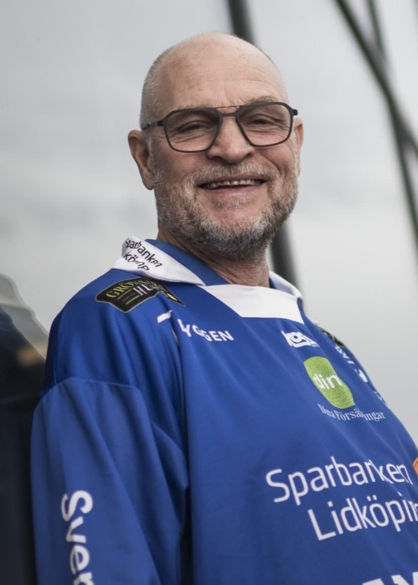 Per Fosshaug iklädd en blå tröja står framför en modern byggnad med glas och stål. Personen speglas i en glasvägg bakom sig under en mulen himmel.