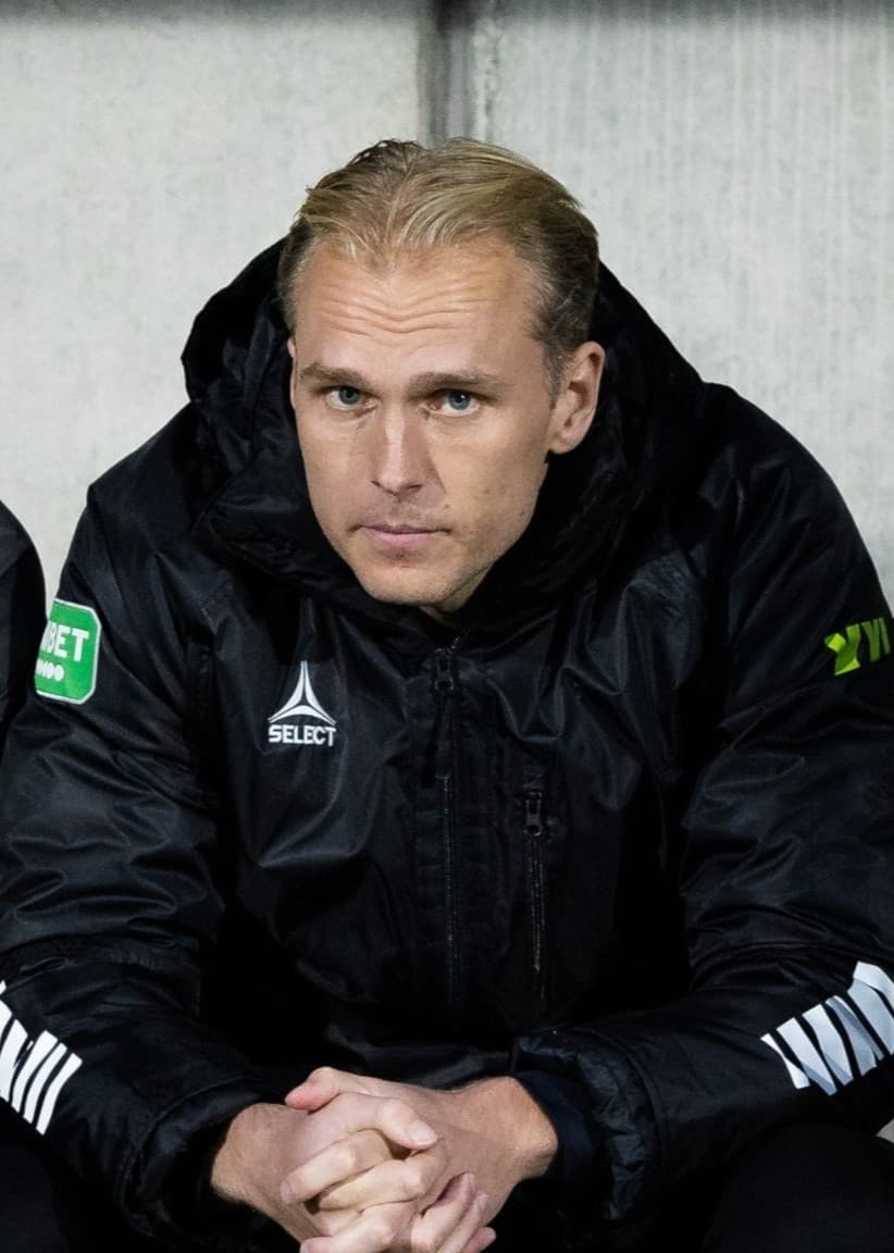 IK Brages tränarduo Janne Mian och William Bergendahl sitter på en avbytarbänk, klädda i svarta tränarjackor med klubbens logotyp, under en match.
