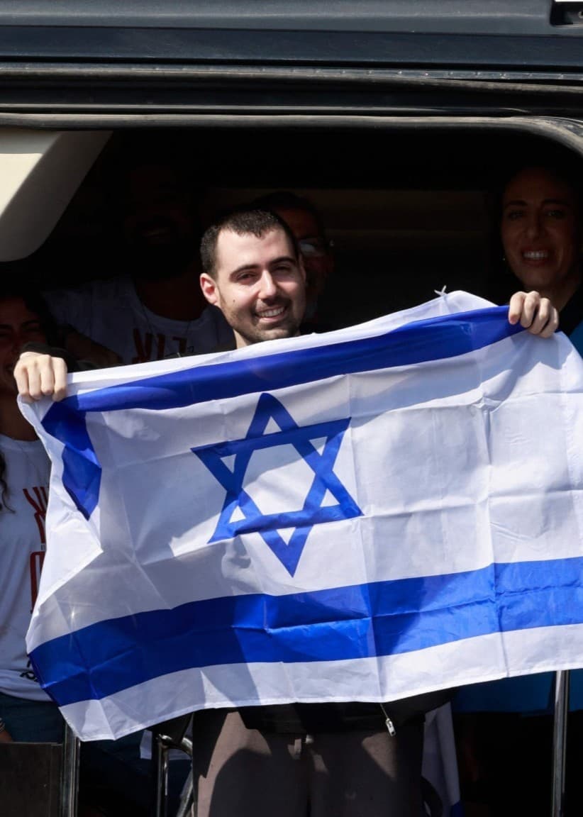 Guy Gilboa-Dalal håller upp en israelisk flagga från ett fordon han färdats i efter att ha släppts ur Hamas gisslan.