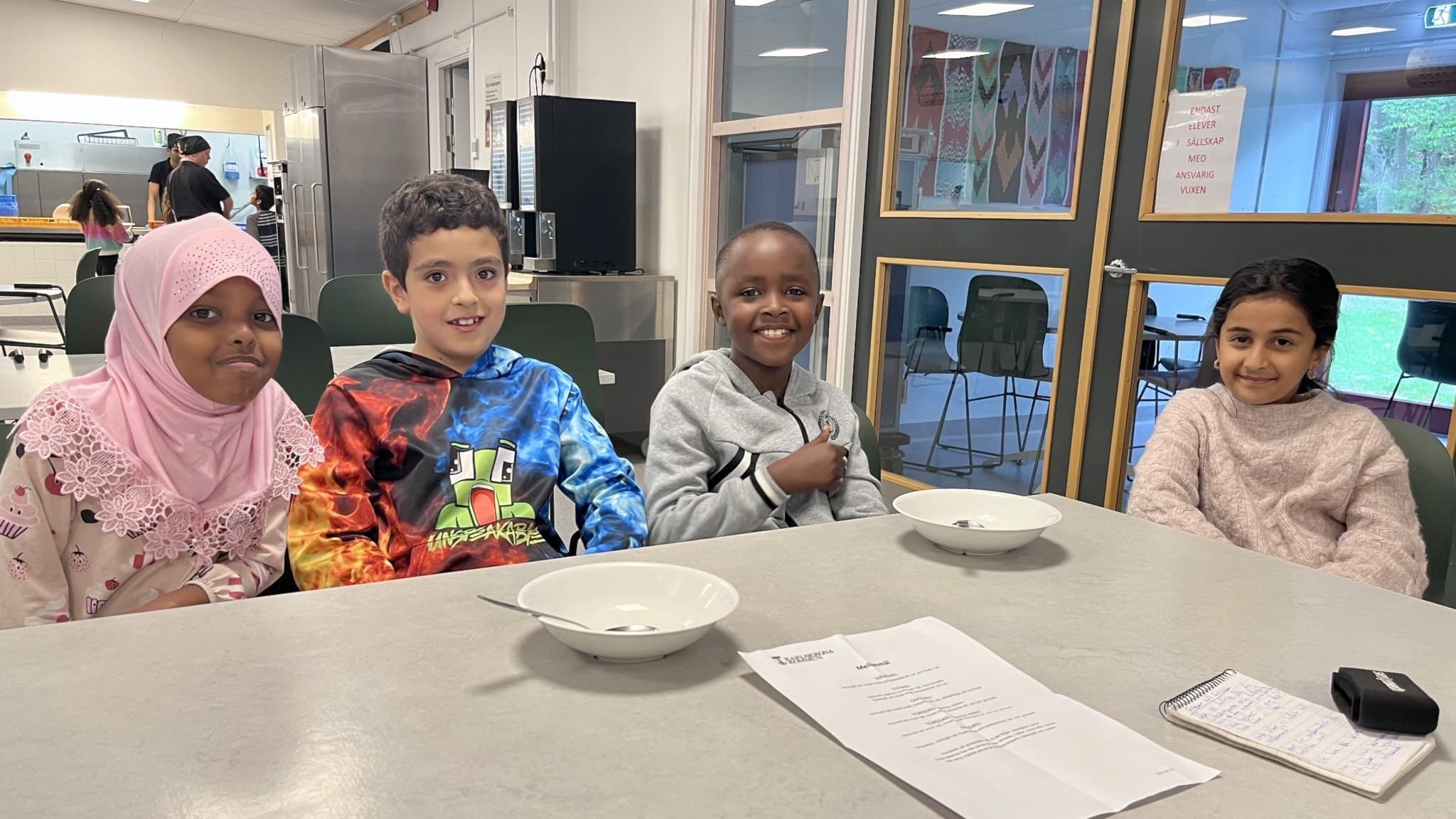 Fyra elever på Sunnadalskolan sitter vid ett bord med tomma tallrikar och ett papper framför sig. De diskuterar olika idéer om vad som är ett bra mellanmål.
