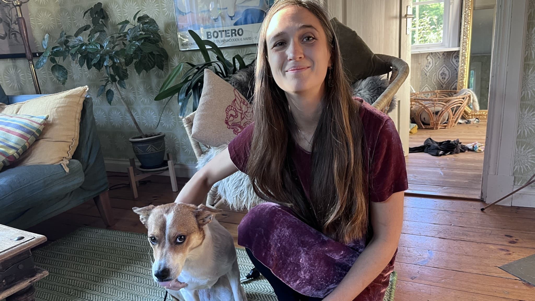 Josefin Molin Björkdal, veterinär och klinikchef på Karlshamns Smådjursklinik, sitter på knä och klappar en hund i ett vardagsrum med trämöbler och växter.