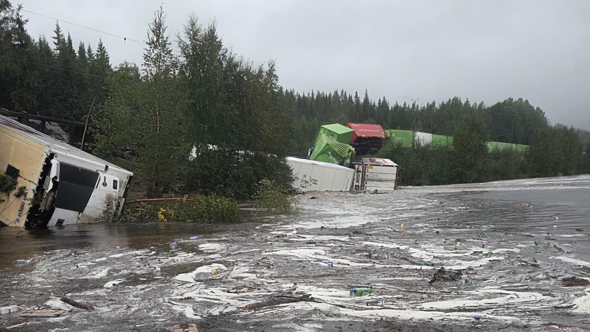 Bild av en tågolycka i Skorped där flera godsvagnar har spårat ur. Vagnen ligger delvis i vatten och omgivningen består av tät skog. Platsen är avspärrad med gul tejp.
