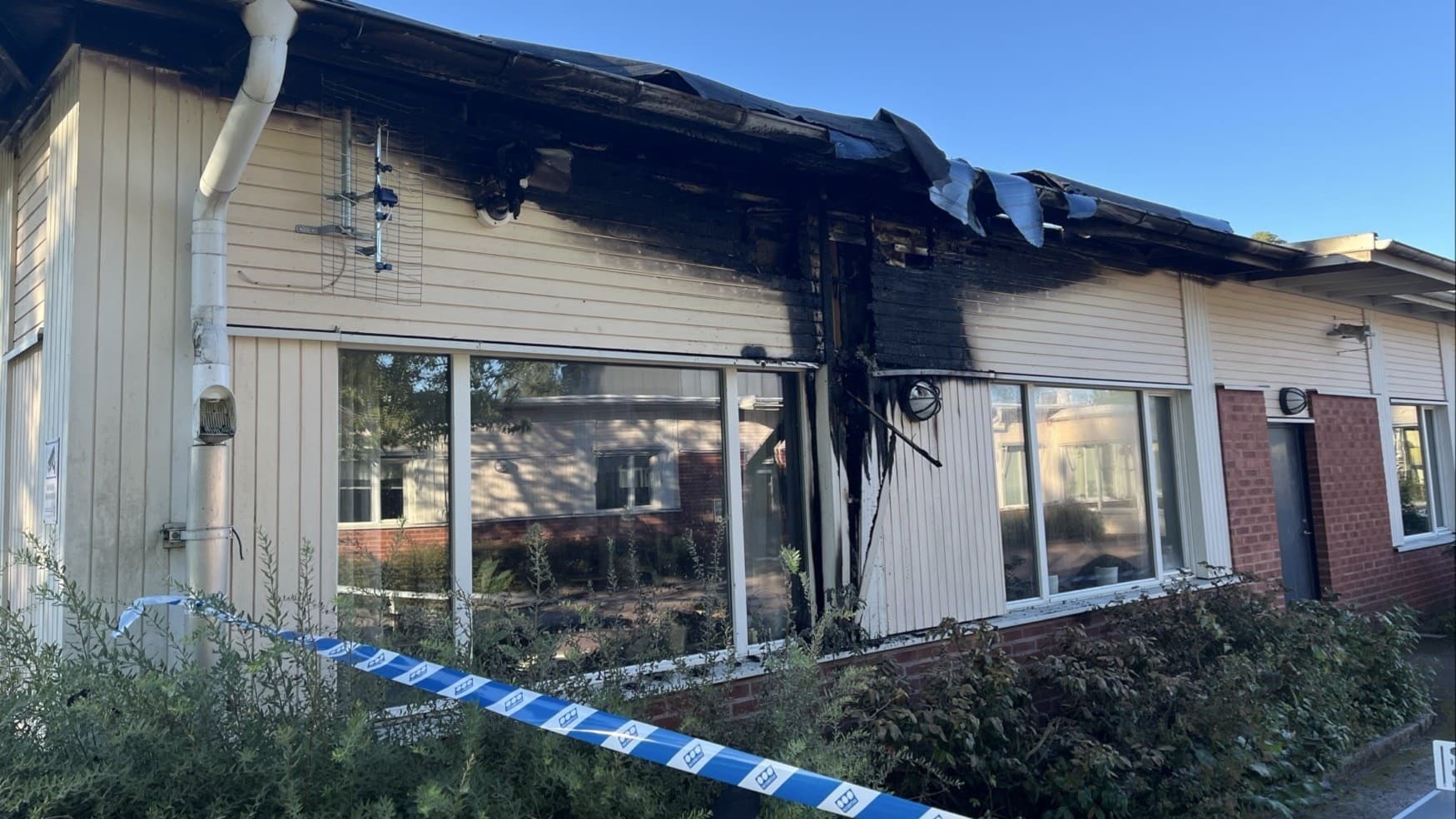 Nybyggeskolan har drabbats av en brand.  Avspärrningsband markerar området, och taket visar tydliga tecken på brandens påverkan.