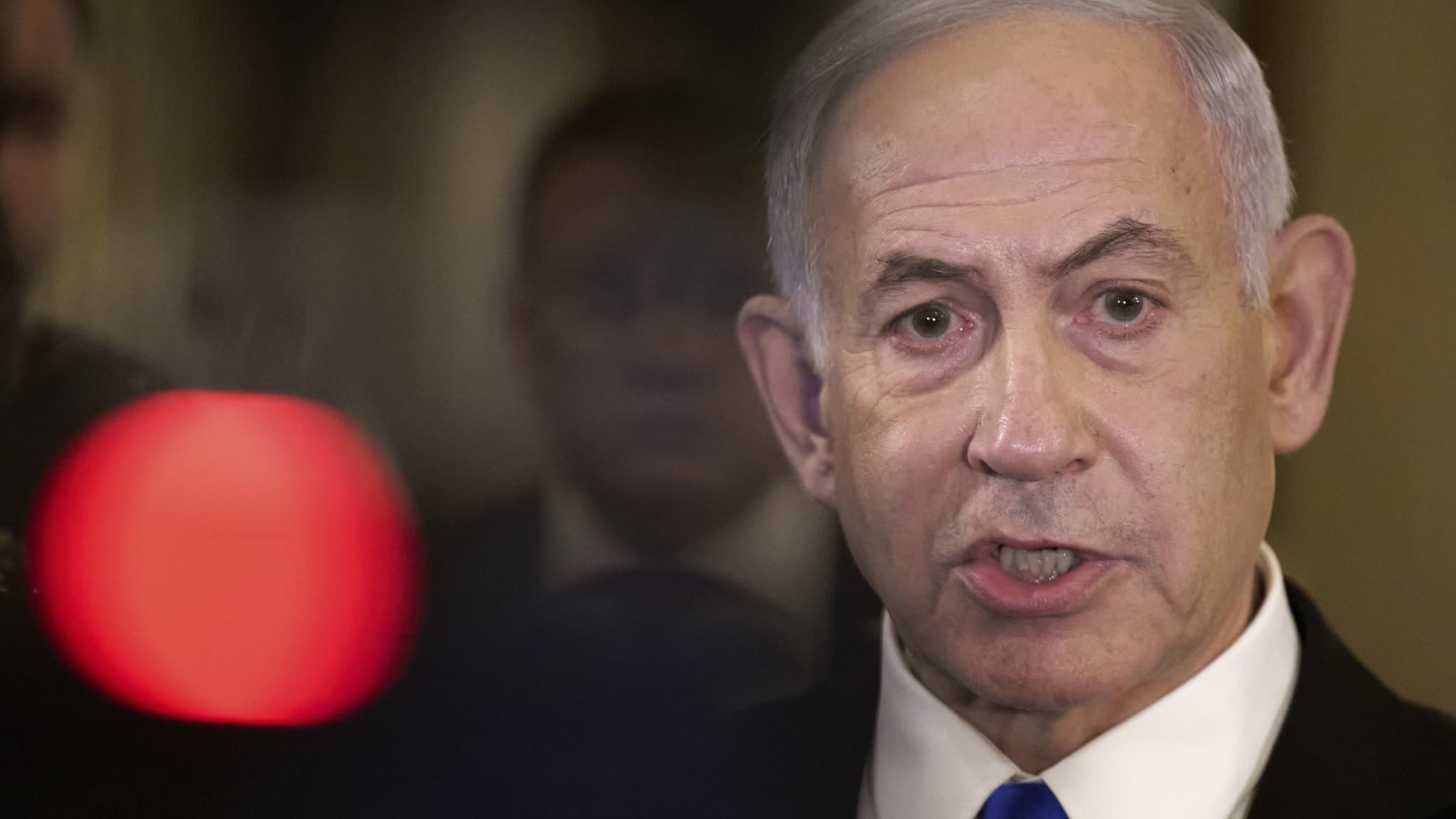 Israels premiärminister Benjamin Netanyahu talar till media på Capitol Hill i Washington. Han bär kostym med blå slips och står i en formell miljö med dämpad belysning.