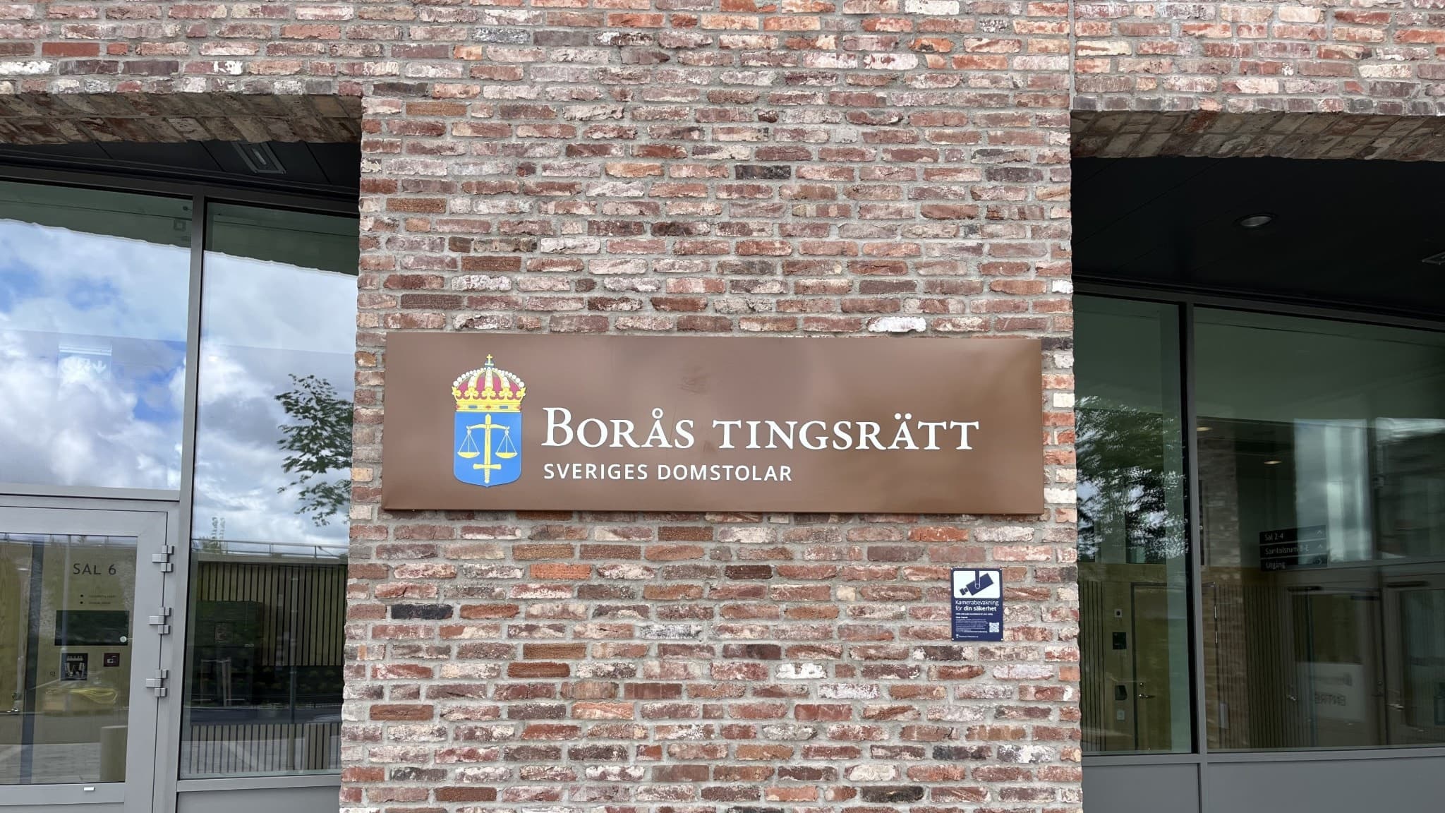 Entrén till Borås nya tingsrätt med en modern fasad av rödbrunt tegel. Skylten visar tingsrättens namn och emblem, med glaspartier som reflekterar omgivningen i bakgrunden.