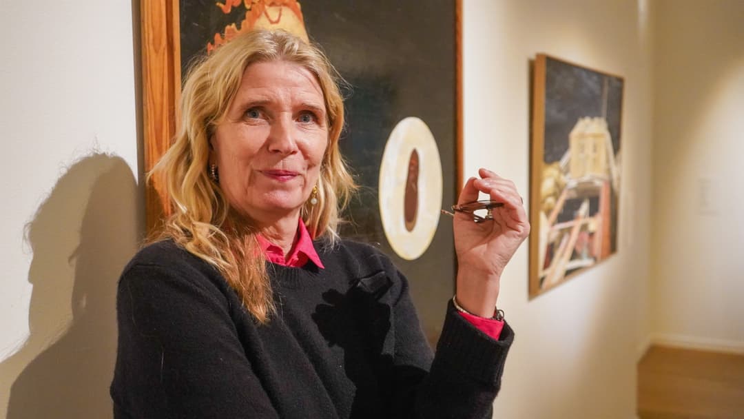 Karin Mamma Andersson, svensk konstnär, står i ett galleri med sina och Ernst Billgrens verk i bakgrunden, som inspirerats av Dick Bengtsson. Hon håller sina glasögon  handen och är klädd i en svart tröja med en röd skjorta under.