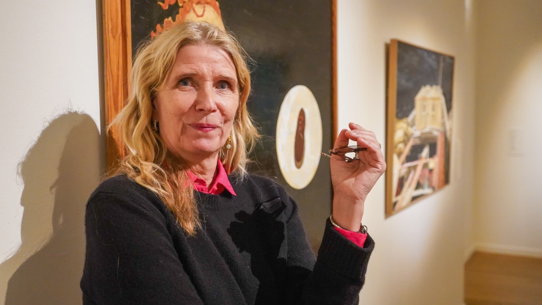 Karin Mamma Andersson, svensk konstnär, står i ett galleri med sina och Ernst Billgrens verk i bakgrunden, som inspirerats av Dick Bengtsson. Hon håller sina glasögon  handen och är klädd i en svart tröja med en röd skjorta under.