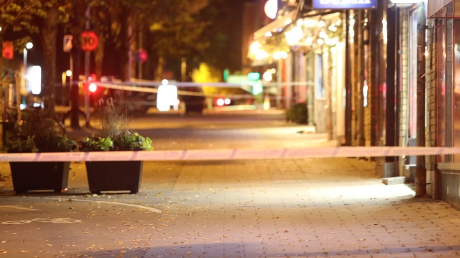 En polisbil står vid en avspärrad gata i centrala Gävle efter en skottlossning. Området är upplyst av gatlampor och flera byggnader syns i bakgrunden.