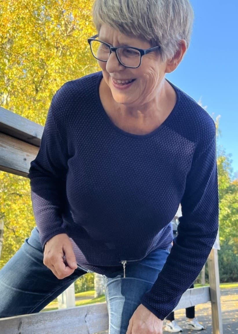 Kvinna med blå tröja utövar seniorparkour genom att huka och ta sig igenom ett staket. I bakgrunden träd med gula höstlöv.