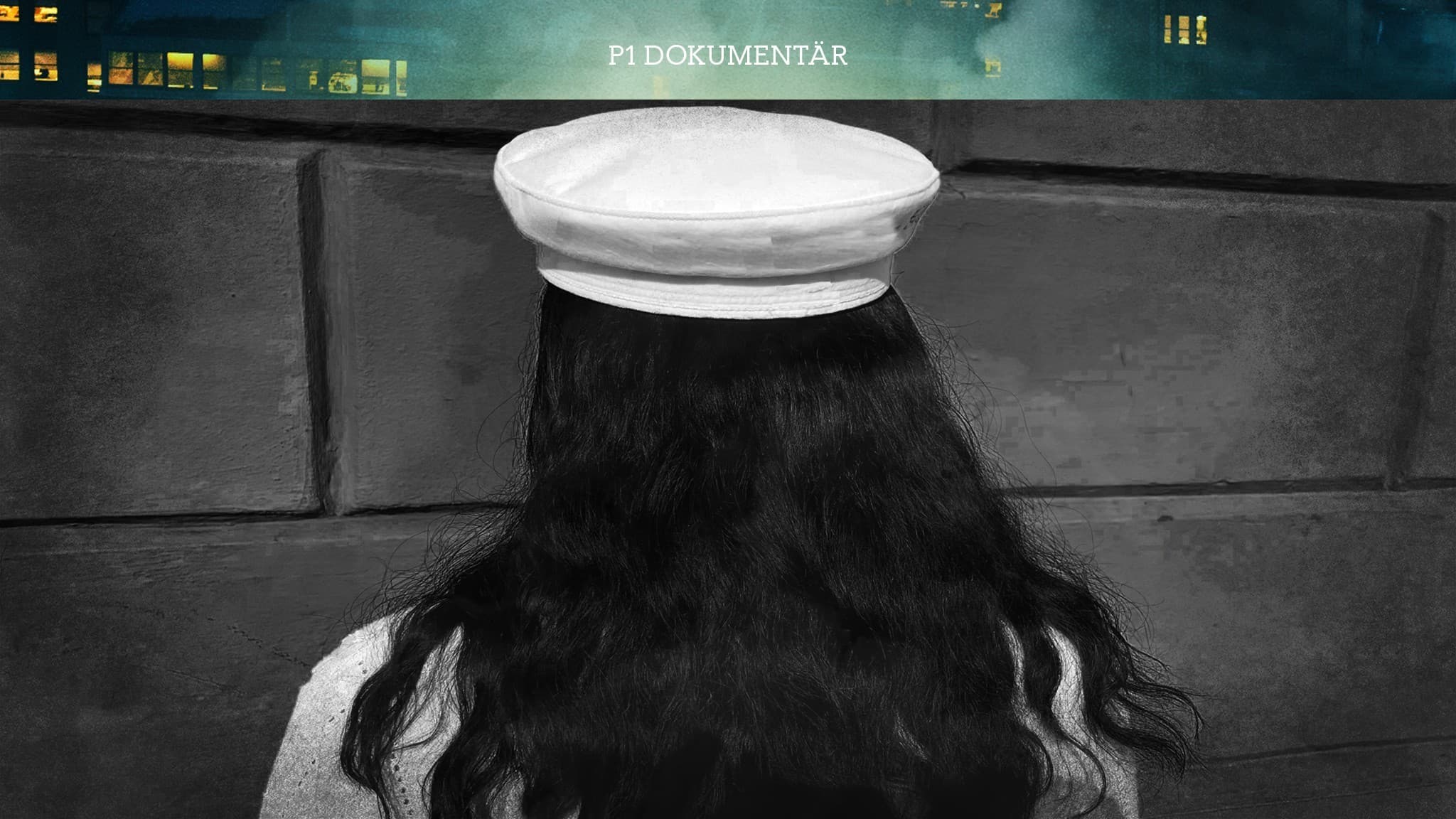 En flicka i studentmössa vid en vägg, bilden är tagen bakifrån.
