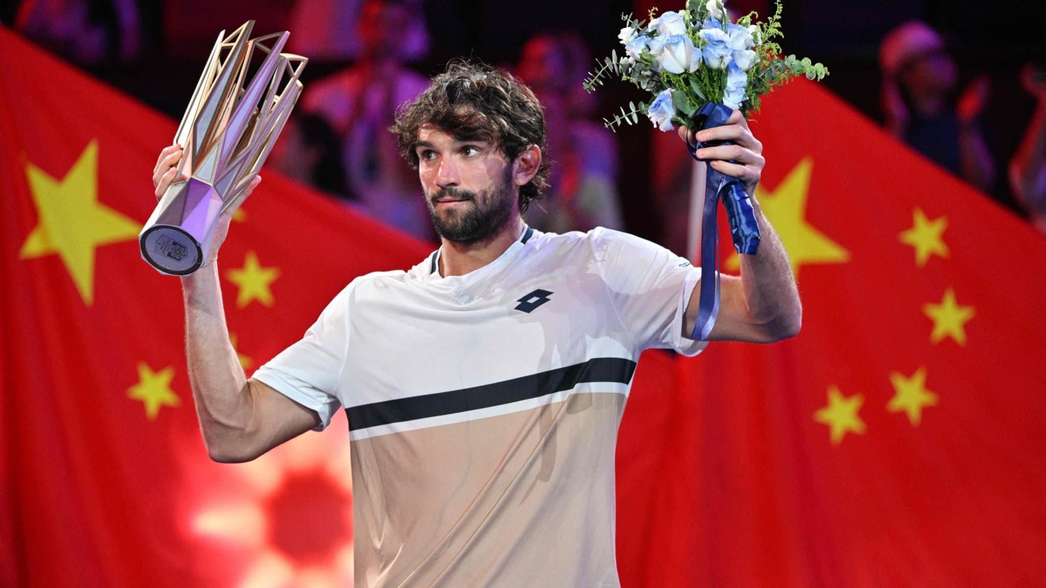 Valentin Vacherot från Monaco firar med en pokal och blombukett efter att ha vunnit herrsingelfinalen på Shanghai Masters tennis i Kina, med kinesiska flaggor i bakgrunden.